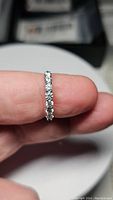 Close-up of the certified moissanite eternity band ring held between fingers showing full band circle of stones.