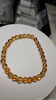 Front view of natural golden citrine round beads on stretchy bracelet placed on a white surface with dark background showing beads and elastic band.