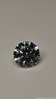 Clear photo showing round brilliant cut loose Moissanite with rainbow reflections and high brilliance on neutral background.