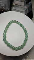 Front view of natural green aventurine round bead bracelet laid out in a circular shape on a white surface.