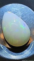 Close-up photo highlighting the pear-shaped opal cabochon with visible rainbow flashes on a dark background.