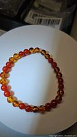 Photo showing the full stretchy bracelet laid flat on a white circular surface, alternating polished round piebald amber and carnelian beads.