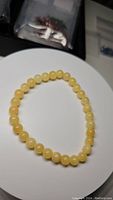 Natural honey calcite bracelet displayed on a white circular surface, showing round polished yellow beads strung evenly on an elastic cord.