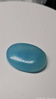 Oval icy blue chalcedony cabochon gemstone on white background showing polished surface and translucent texture.