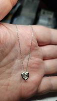 Close-up photo of sterling silver rhodium plated chain and heart pendant necklace with a small moissanite stone held in palm showing detailing.