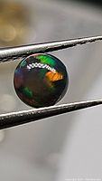 Close-up of one side of the round black opal showing vibrant flashes of green and orange with smooth polished surface.