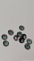 Ten round calibrated Mystic Topaz loose gemstones with visible green, purple, and blue iridescence laid out on a white surface.