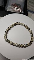 Photo showing a circular stretchy bracelet composed of round, spotted dalmatian jasper beads on a light surface.