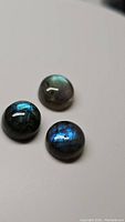 Three round polished natural labradorite cabochon stones showing blue and green flashes on dark bases.