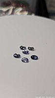 Six oval cut natural tanzanite gemstones displayed on white surface, showing their size, shape, and blue-violet color.