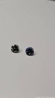 Photo showing two round cut tanzanite stones on white background: one blue-purple and one green.