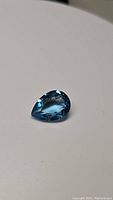 Pear-shaped natural Swiss blue topaz gemstone on a white background, showing color and clarity.