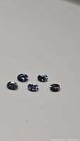 Five oval calibrated natural untreated tanzanite gemstones, purple-blue color, arranged on a plain surface.