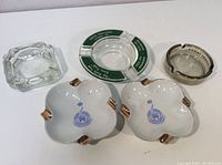 Top view showing all five ashtrays in assortment, including white ceramic, clear glass, and branded ashtrays