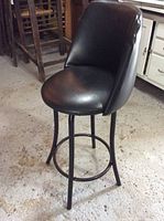 Front angled view of black counter height stool showing padded seat and backrest, metal legs, footrest ring, and overall shape.
