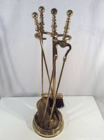 Full view of brass fireplace tool set with stand showing four tools inserted.