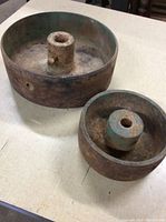 Large and smaller heavy metal wheels side by side on a table showing surface rust and wear