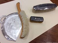 Three table brushes and a silver look tray arranged on a plain surface.