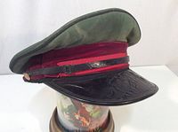 Side angle of the vintage military style cap showing the green top, red band, black leather strap, and gold button on side