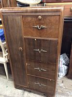 Front view of the vintage wooden armoire showing four drawers with decorative metal handles and a side cabinet door.