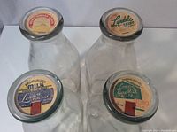 Top view of 4 glass milk bottles with metal lids showing vintage logos for Prince Edward Dairy Cream, Lyndale Dairy, and London Pure Milk Co Ltd.