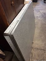 Side view of grey Arborite laminate tabletop showing thickness and metal edging detail.