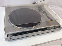 Full view of turntable with closed clear plastic dust cover, showing platter, tonearm, and body.