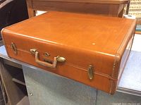 Full closed view of the brown leather suitcase showing its rectangular wedge shape and leather texture.