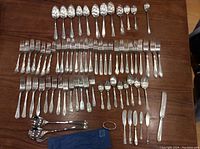 Wide view of entire silverware collection arranged on a table showing forks, spoons, knives, and the blue Birk's pouch with salad utensils.