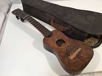 Full view of vintage wooden ukulele and worn vintage case including leather strap and floral lining.