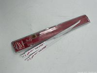 Two white Milwaukee Sawzall blades with tooth pattern for cutting wood with nails, laying atop red and clear Milwaukee plastic blade case.