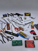 Full spread of assorted hardware tools including scissors, wrenches, clamps, level, pliers, leather pouch, and boxed staples.