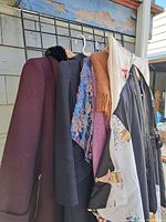 Vintage outerwear and shawls hanging on rack including coats, mohair shawl, and scarf.
