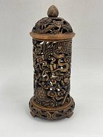 Front view of the carved stone candle holder showing intricate openwork with floral and bird motifs and a finial on top.