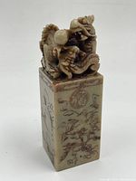 Front view of dragon carving atop the base with visible engraved motifs on the side of the statuette.