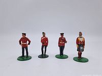 Front view of four hand-painted toy soldiers standing in a row on green bases against a plain background.