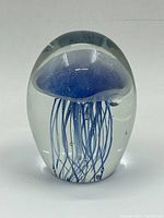 Front view of a clear glass paperweight with a blue jellyfish inside, showing tentacles and dome-shaped bell.