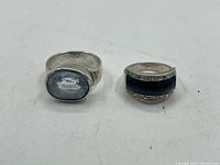 Front view of two vintage rings on white background, one with oval blue stone and the other with black inlay and marcasite accents.
