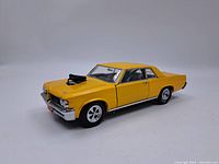 Front-side view of yellow Pontiac GTO model car showing side and front details including hood with engine protruding.