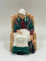 Front view of the Royal Doulton figurine showing an elderly woman sitting in a patterned armchair, wearing a white bonnet and green shawl with a black cat seated at the base.