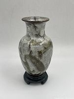 Front view of ceramic vase on stand showing oval shape and abstract glaze pattern.