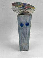 Full view of the stained glass sculpture showing the colorful circular top with geometric divisions and the light blue base with blue glass spheres.