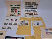 Wide overview of multiple stamp album pages, yellow envelopes with grouped stamps, and loose stamps on the table.