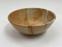 Side view of a polished stone bowl showing natural color variations and cracks.