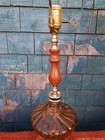 Side view of vintage lamp showing the amber glass base, wooden midsection and brass socket with turn-key switch, and brass harp.