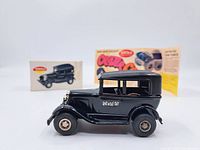 Side view of the vintage Tonka Rat-A-Tat-Tat toy car in black with original box and flyer behind it.