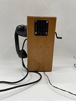 Side view showing the wooden box with speaker grille and black handset attached by cord, with wires coming out of bottom.