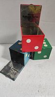 Three dice-shaped metal tins stacked, showing open lid of red tin with reflective interior and Holland Toffee brand inside lid.