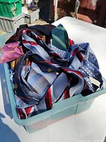 Multiple men's neck ties with various patterns and colors piled inside a translucent plastic bin.