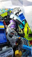 Photo showing a mix of toy cars including green, blue, silver, purple, and yellow vehicles piled together.